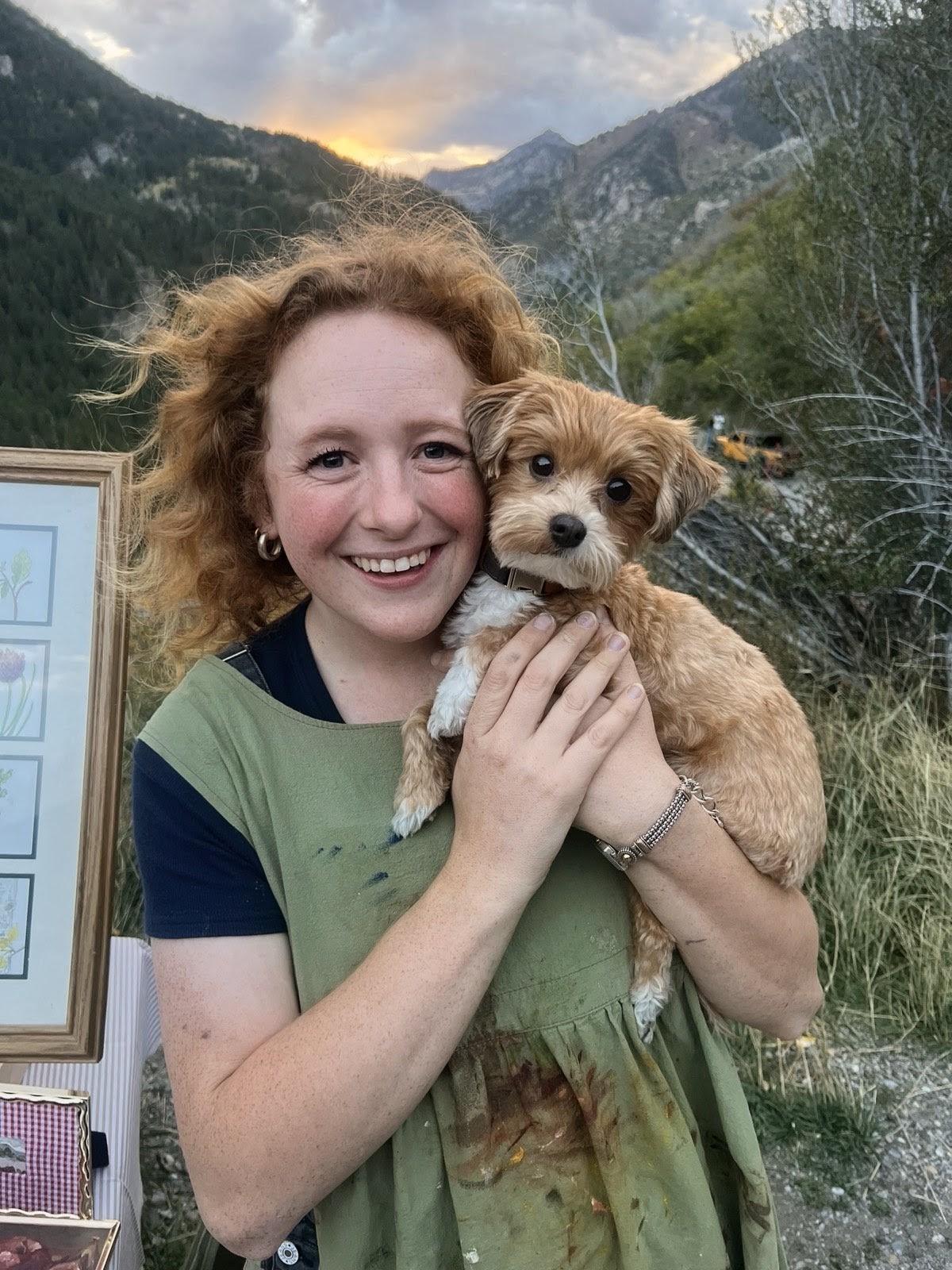 Mary Kate holding a small dog outdoors with mountains behind them.