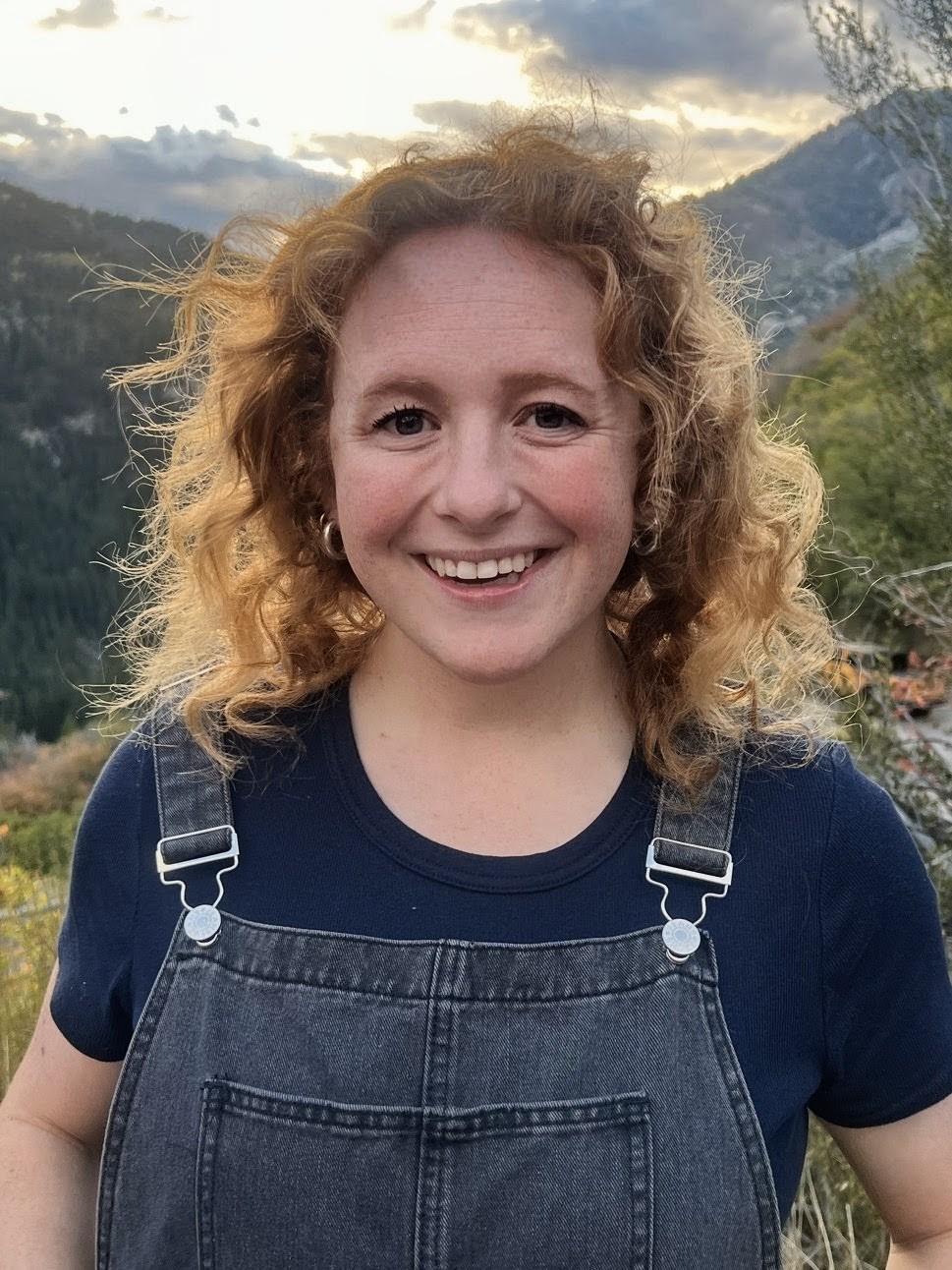 Mary Kate smiling outdoors with mountains behind her.